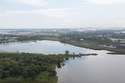  Aerial view of a lake surrounded by wetlands, with a city in the background.