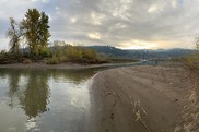 A riverbank of brown soil gives way to a tree-covered island, with a mountain sunset in the background.