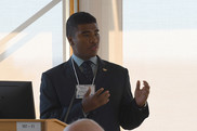 A high school student standing at a podium delivers a presentation. He is wearing a blazer and tie.