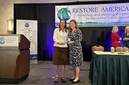 Ciona Ulbrich receiving award from Carrie Robinson on stage at the Restore America's Estuaries Summit.