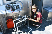 A college student smiles as she works to connect a camera to a frame made out of PVC pipe.