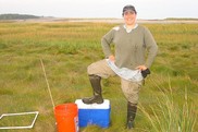 Genevieve Bernatchez stands triumphant in green marsh on the last sampling day of her graduate career
