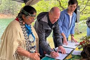 Three people signing documents on a table by a river bank. Credit: Jessica Abbe