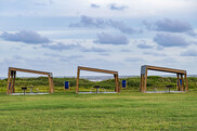 Three brown, asymmetrical picnic shelters sit in a row in front of beach dunes. Credit: Texas Parks & Wildlife Department