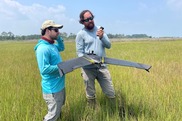 Two men stand in a field; one is holding a large fixed-wing drone they are about to launch. Credit: NOAA Office for Coastal Management
