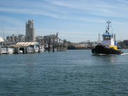 A tugboat navigates a river with an industrial shoreline behind it.