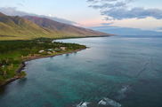 Aerial view of a shoreline with coral reefs in the foreground and mountains in the background