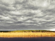 A sunlit prairie sits in the background behind calm water.