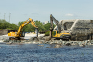 Two heavy construction machines demolish a dam.