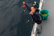 Field scientist Nicole Ferreira holds a baited hook and line survey jigger line with a small black sea bass hooked on it.