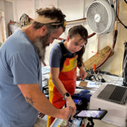 Two people stand in front of a squid processing station to measure a squid.