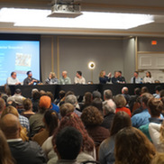 Several people sitting in a conference room listening to a panel discussion.