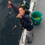  A scientist stands at the gunnel of a recreation fishing vessel and holds a baited fishing line with several hooks.
