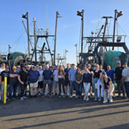 Many people standing in front of commercial fishing vessels.
