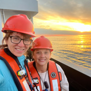 Two field scientist at sunrise on ship wearing hardhats and lifevests