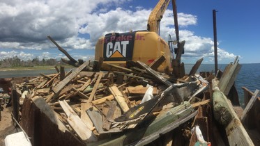 Large piece of construction equipment is behind a pile of collected lumber. 