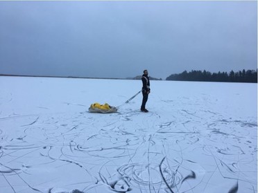 A person stands on a frozen lake pulling a sled.