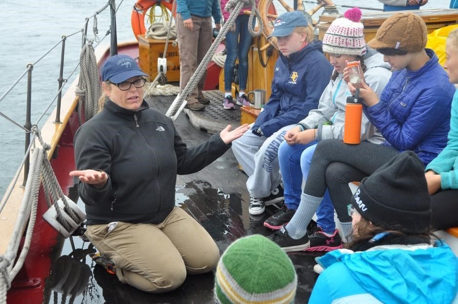 A teacher leads a group of students in discussion aboard a ship. 