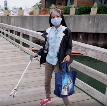 Ocean Today host Symone holding a reusable bag and trash-grabber on a pier in Baltimore, MD.