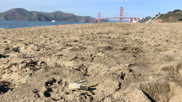 Plastic shotgun wad debris on a beach with the San Francisco Golden Gate Bridge in the distant background.