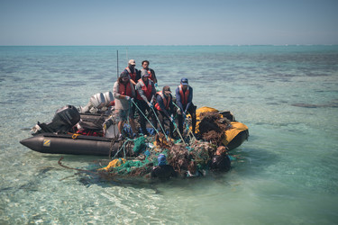 A marine debris removal team pulls a large derelict net mass out of the water at Midway Atoll.