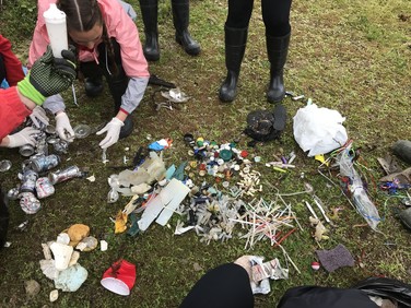 Assorted plastic debris collected and organized in piles on the ground by a small group of people.
