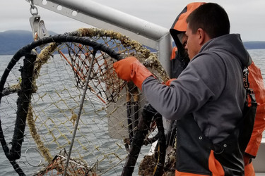 Two removal team members pull a derelict crab pot aboard a boat. 