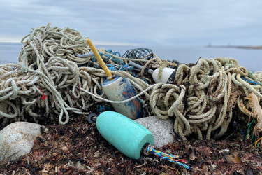 A mound of derelict fishing gear found on a rocky ocean shoreline.