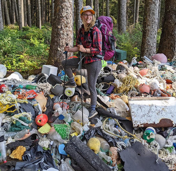 Hillary Burgess, Marine Debris Program monitoring coordinator, standing with hiking poles and backpack atop a pile of debris.