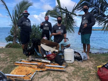 Four people wearing Hawai'i Marine Animal Response shirts standing proudly over a pile of debris.