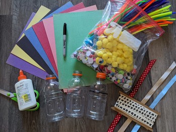 Supplies for the craft laid out (construction paper, beverage bottles, glue, scissors, googly eyes, scrap ribbon, and a permanent marker).