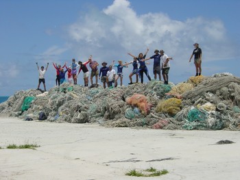 A group of people stand triumphantly on top of a pile of derelict nets removed from sensitive habitats.