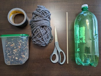 The supplies needed to create a plastic bottle bird-feeder laid out on the table (supply list below).
