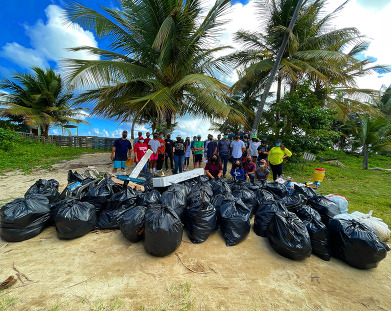 A large group of volunteers stand behind a large pile of trash bags and other debris removed from Puerto Rico shorelines.