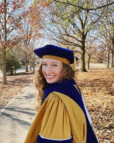 Dr. Madison Willert, 2023 Knauss fellow in her graduation cap and gown with fall foliage in the background.