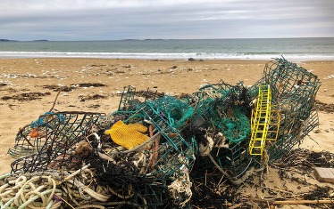 A tangled pile of derelict fishing gear on the shoreline with waves in the distance.