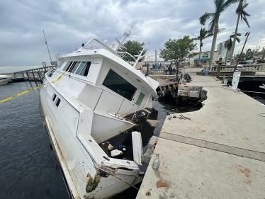 A half sunken vessel that crashed into a marina walkway, surrounded by debris and marked off with caution tape.