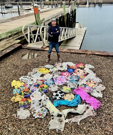 A man standing behind a pile of mylar balloons laid out on the ground that were collected from fishermen.
