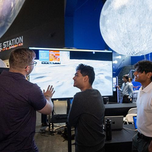 A man showing two students an image of the moon's surface on a large TV screen