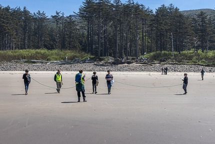 Students with Teacher wearing flourescent vests on a Pacific Northwest Beach with pine trees in the background.