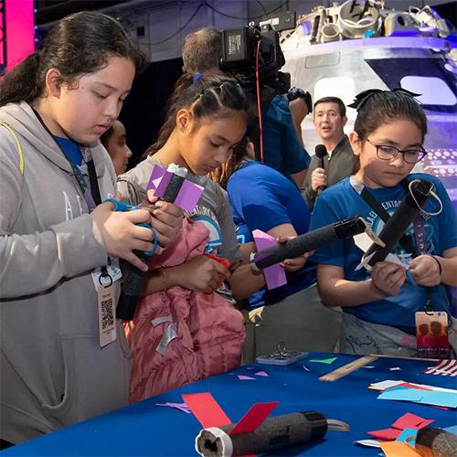 Three girls building model rockets at a NASA event