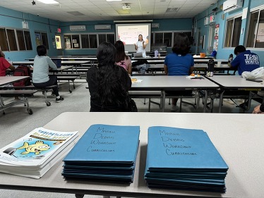 A presenter speaking to a classroom with a stack of marine debris curricula piled on one of the desks.