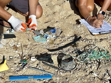 Two people sorting through marine debris on a sandy beach.