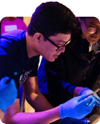 Two students looking at a test tube while wearing safety glasses