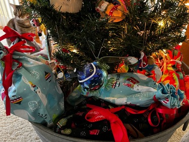 Presents wrapped under a Christmas tree in resuable bags with ornaments hung on the tree.