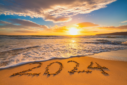 2024 written in the sand as waves threaten to wash the numbers away in front of a setting sun