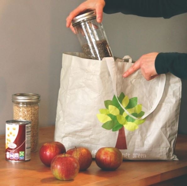 Someone putting glass jars filled with grocery items, canned goods, and apples into a reusable bag.