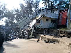 A dilapidated house structure on a tropical, sandy shoreline.