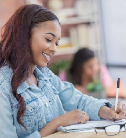 Woman at a desk smiling and writing with a pen