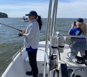 Woman fishing off of a boat in choppy waters.